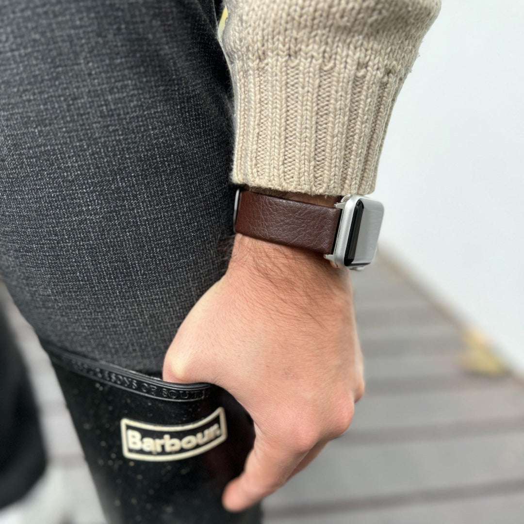 Dunkelbraunes veganes Weinleder-Armband für Apple Watch – Schrägansicht mit Gummistiefeln im Hintergrund, stilvoller Outdoor-Look