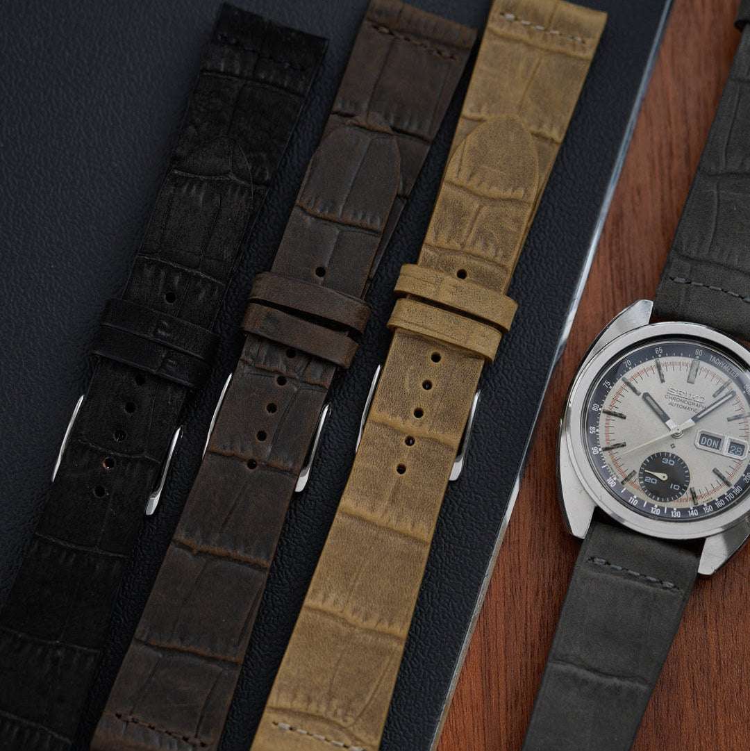 Graues Krokodilprägung Uhrenarmband an Seiko Automatic, nebeneinander mit drei weiteren Krokodilprägung Uhrenarmbändern – Detailaufnahme von vier exklusiven Uhrenarmbändern aus hochwertigem Leder mit luxuriöser Krokodilprägung, ideal für sportliche und elegante Uhren