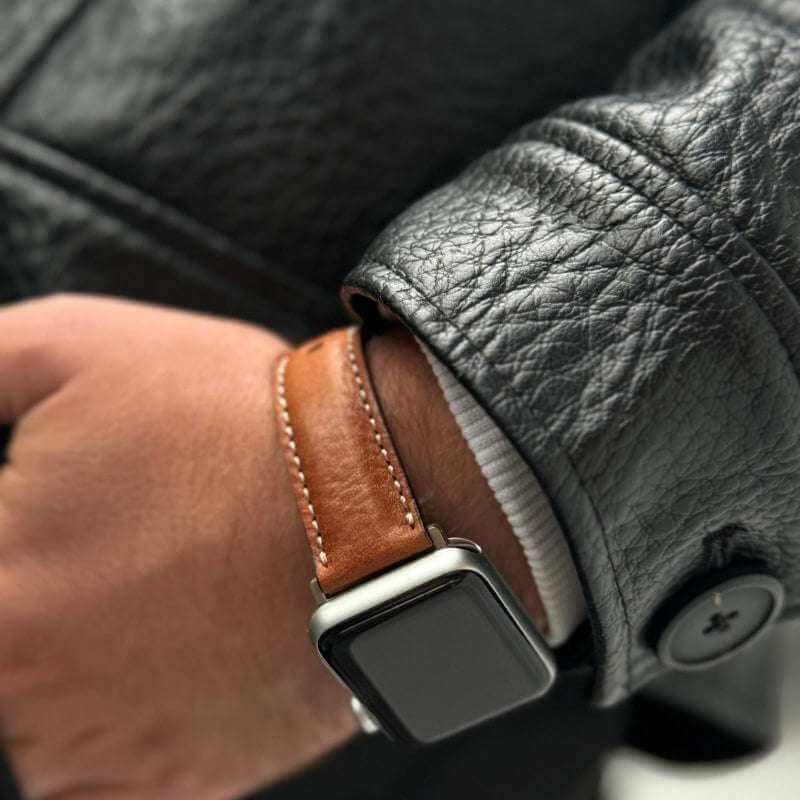 Detailaufnahme des getragenen Apple Watch Ultra 2 Armbands Leder in Hellbraun, kombiniert mit einer Lederjacke.