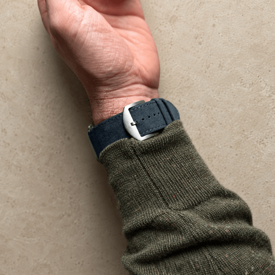 Alcantara – Apple Watch Armband in Dunkelgrau am Handgelenk eines Mannes, kombiniert mit einem grünen Pullover.