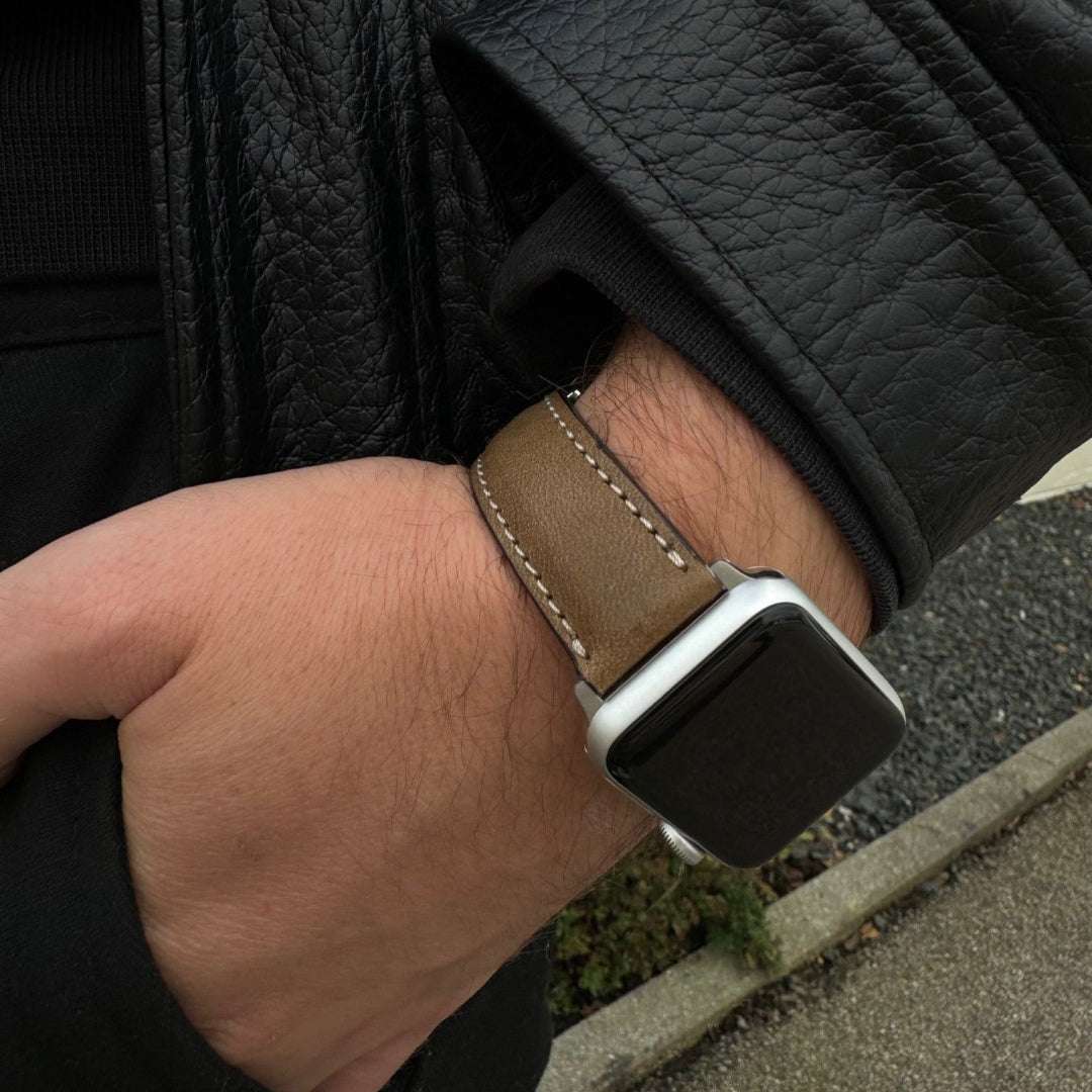 Handgelenk mit Apple Watch 8 Armband Leder in Braun, kombiniert mit einer schwarzen Jacke.