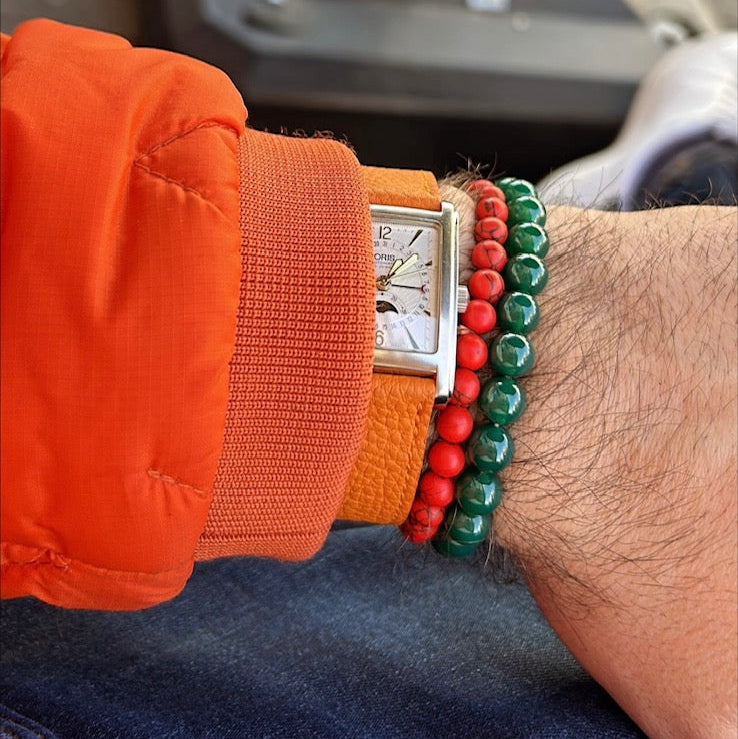 Detailaufnahme eines Handgelenks mit einem orangefarbenen Uhrenarmband leder herren, umgeben von bunten Armbändern und einer elegant gearbeiteten Uhr, die Stil und Komfort vereint.