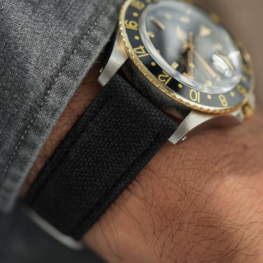 Schwarzes Canvas-Uhrenarmband an einer Rolex Oyster Perpetual in Schwarz-Gold, getragen am Handgelenk, sportlich-eleganter Stil