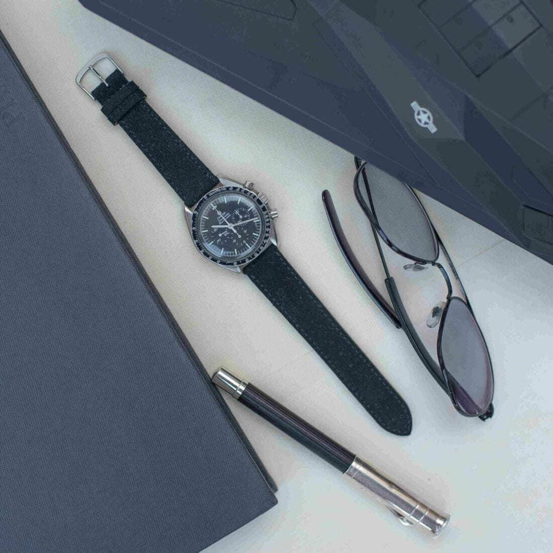 Schwarzes Nizza Velourslederarmband von oben an einer Omega Speedmaster fotografiert, das die hochwertige Verarbeitung und die stilvolle Verbindung von Uhrenarmband und klassischer Uhr betont.
