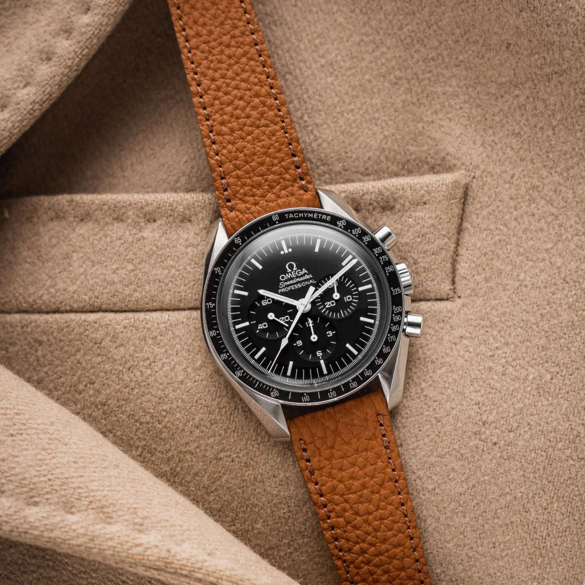 Whiskyfarbenes Deauville Uhrenarmband aus Togoleder an Omega Speedmaster auf einer Jacke liegend