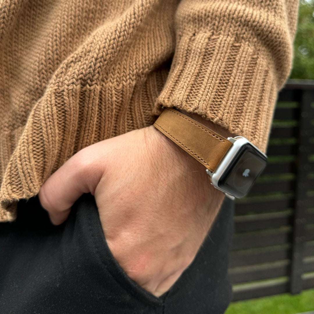 Whiskyfarbenes Nubukleder-Armband für Apple Watch am Handgelenk – Schrägansicht mit braunem Pullover, stilvolle Detailaufnahme